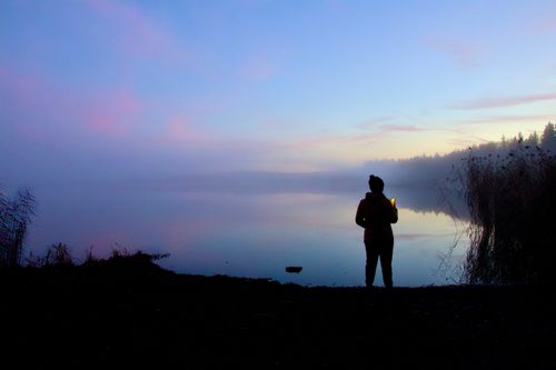 Free Silhouette of a person by a misty lake at twilight with a serene and tranquil atmosphere. Stock Photo