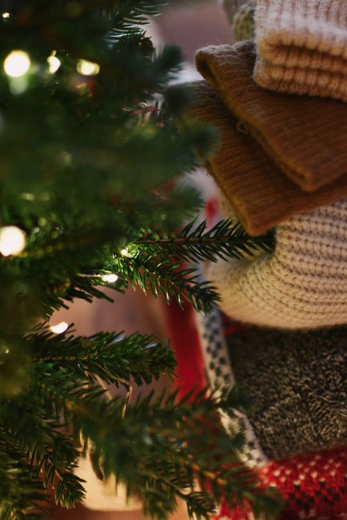 Free Stack of cozy sweaters next to a Christmas tree, perfect for holiday warmth. Stock Photo