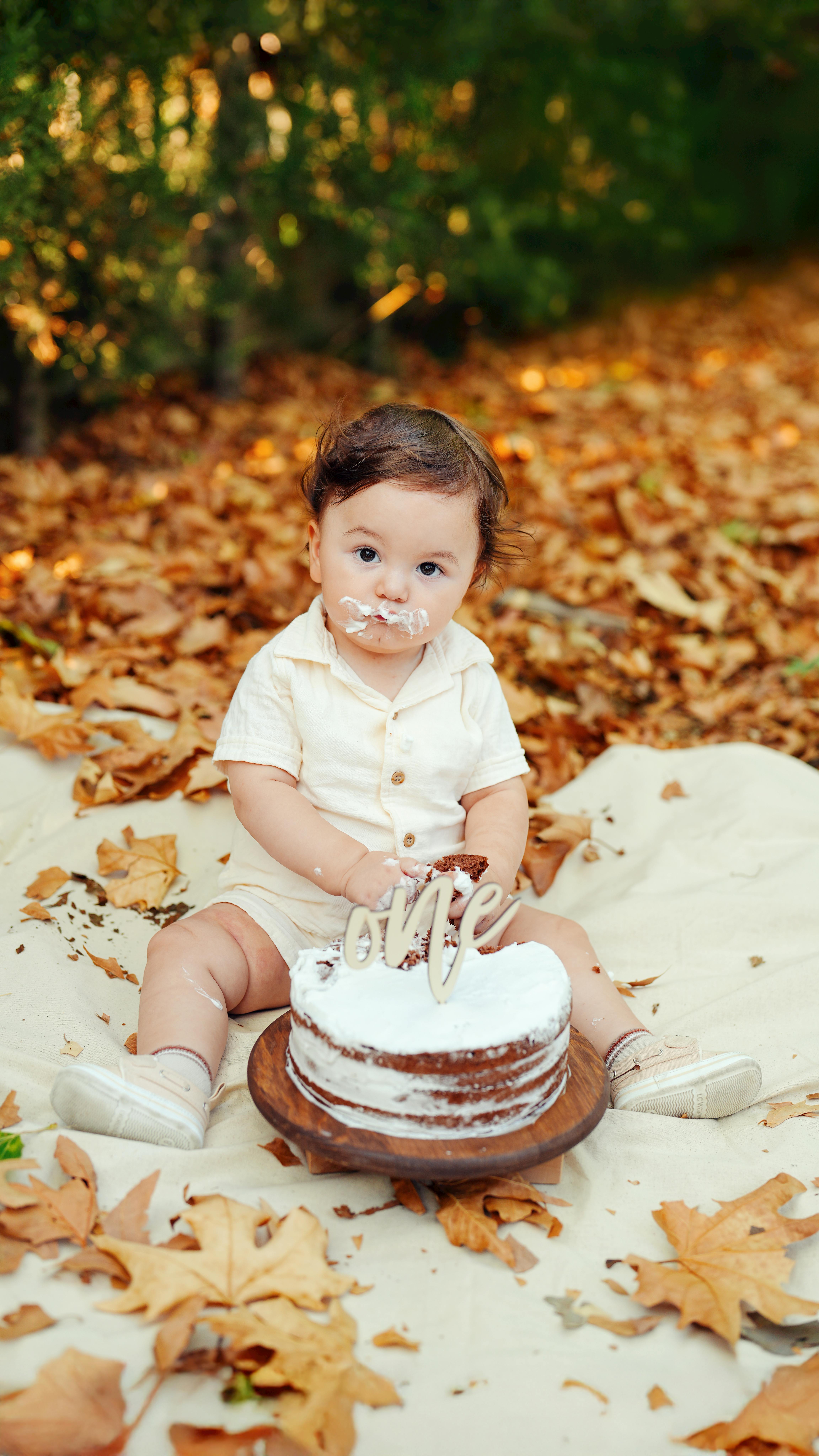 Cute baby enjoys first cake smash in a picturesque autumn setting with fallen leaves.