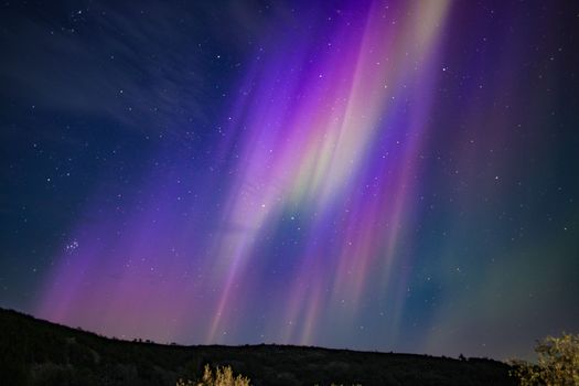 Stunning display of the Aurora Borealis over a remote landscape with vivid purple and green hues lighting up the night sky.