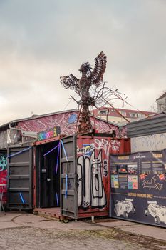 Metal bird sculpture atop graffiti-covered container in artistic, urban setting.
