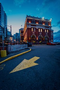 Vivid dusk scene in downtown Vancouver showing a yellow arrow and illuminated historic building.