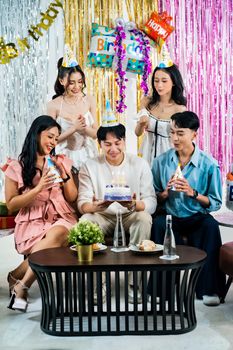 Friends celebrate a birthday with cake and party hats indoors in Jakarta.