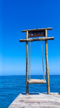 A simple wooden swing on a pier with a vivid blue Caribbean Sea background in Bolívar, Colombia.