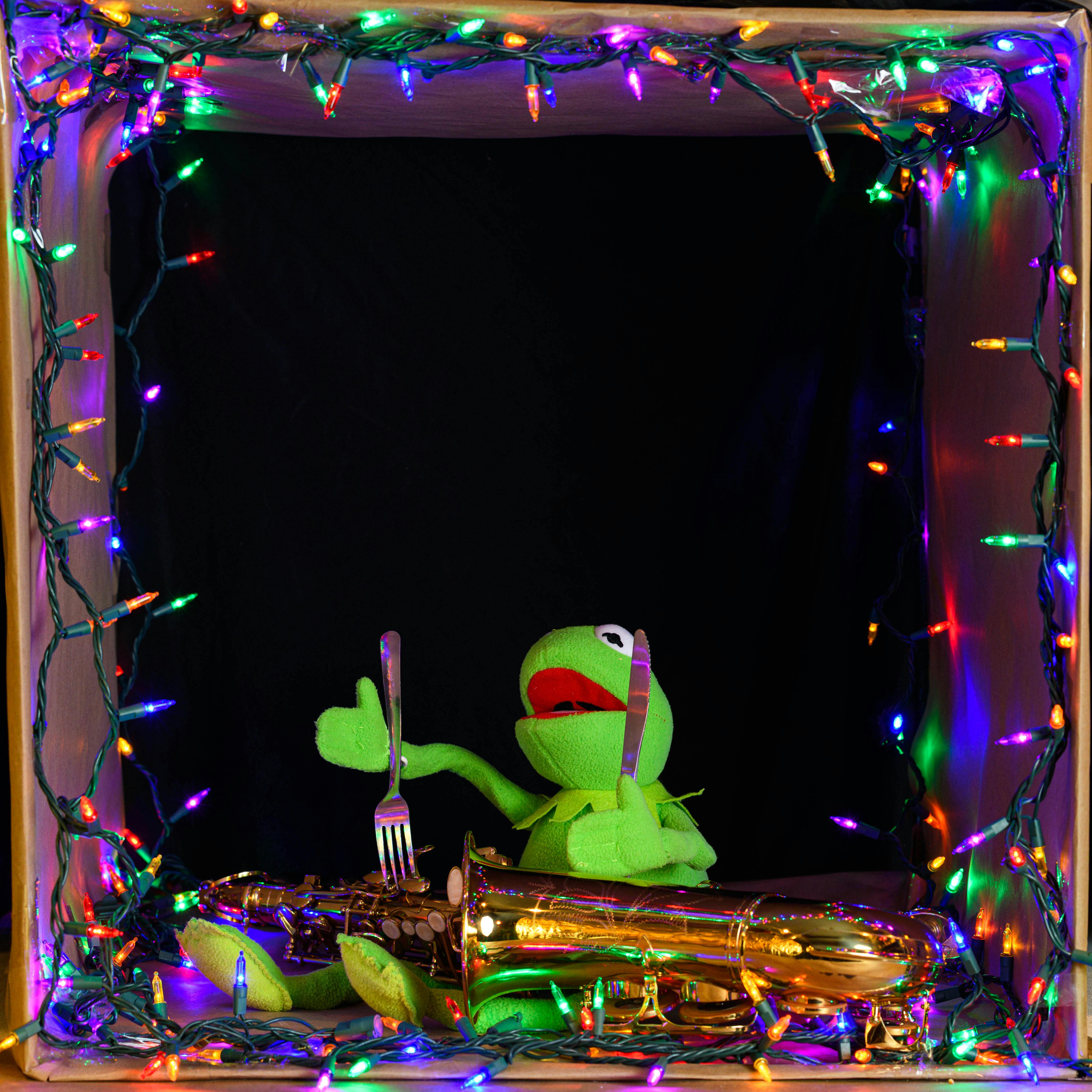 Green puppet holding cutlery with saxophone surrounded by colorful lights.