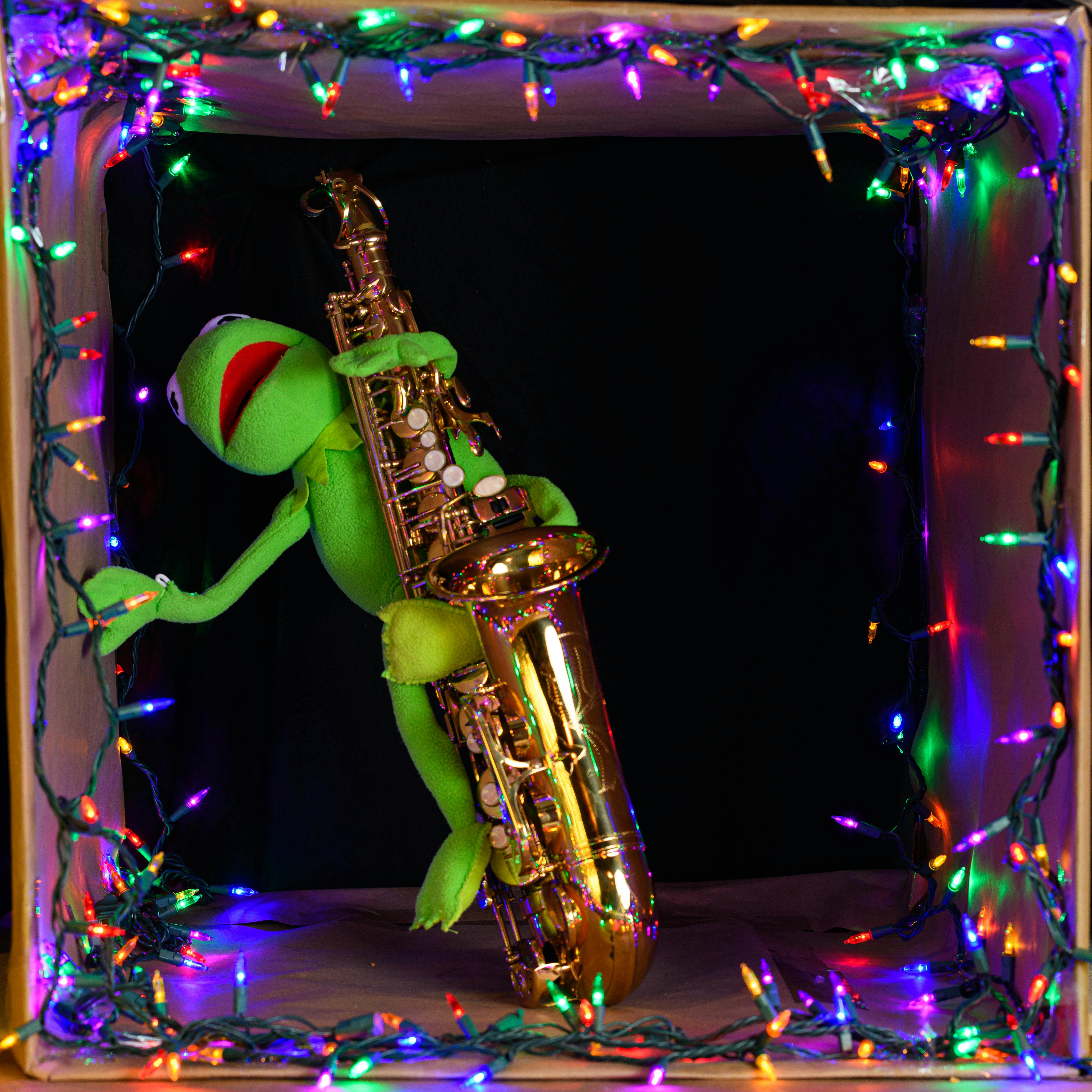 Green puppet playing a saxophone, surrounded by vibrant holiday lights in a playful scene.