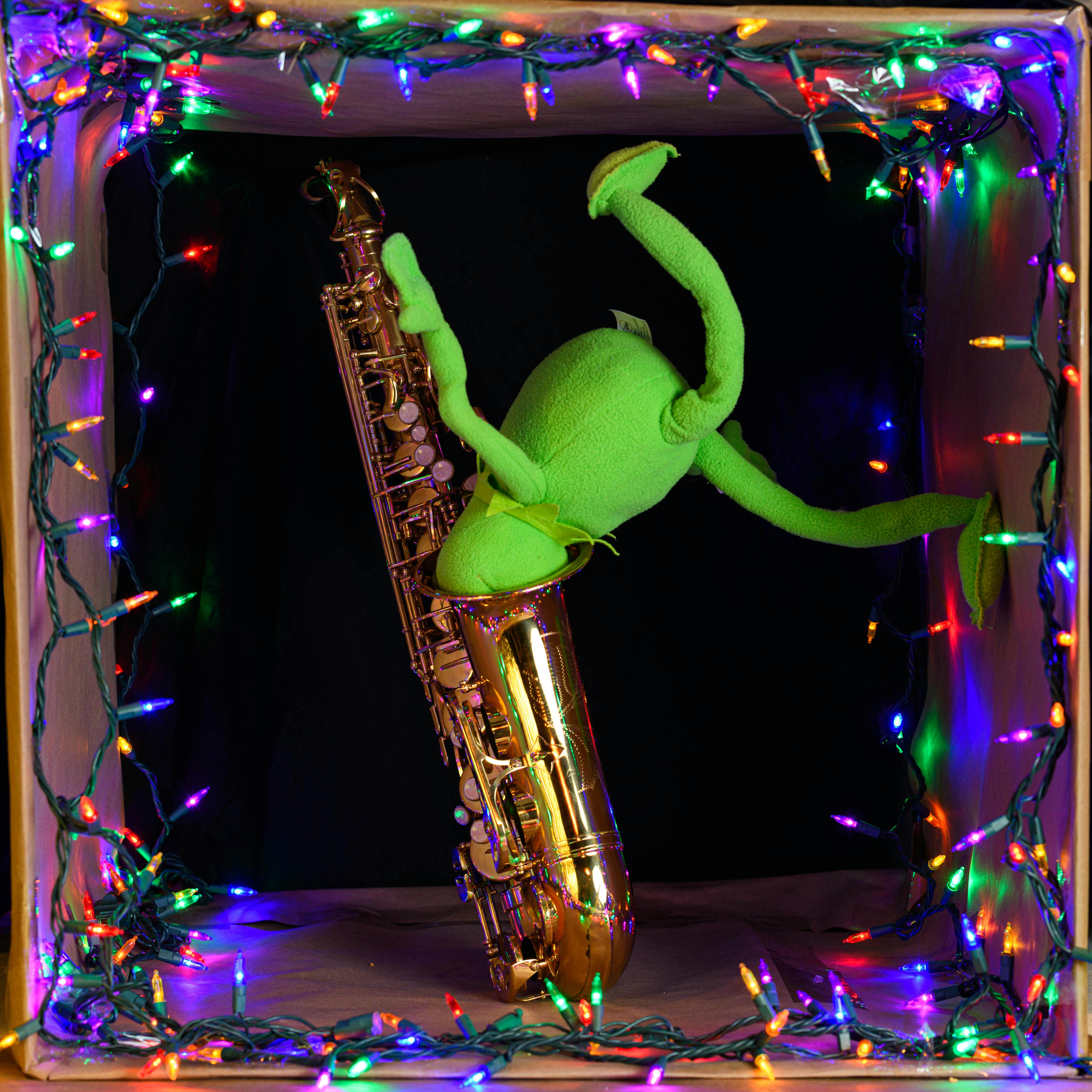 Green puppet playing saxophone amid vibrant Christmas lights for a festive display.