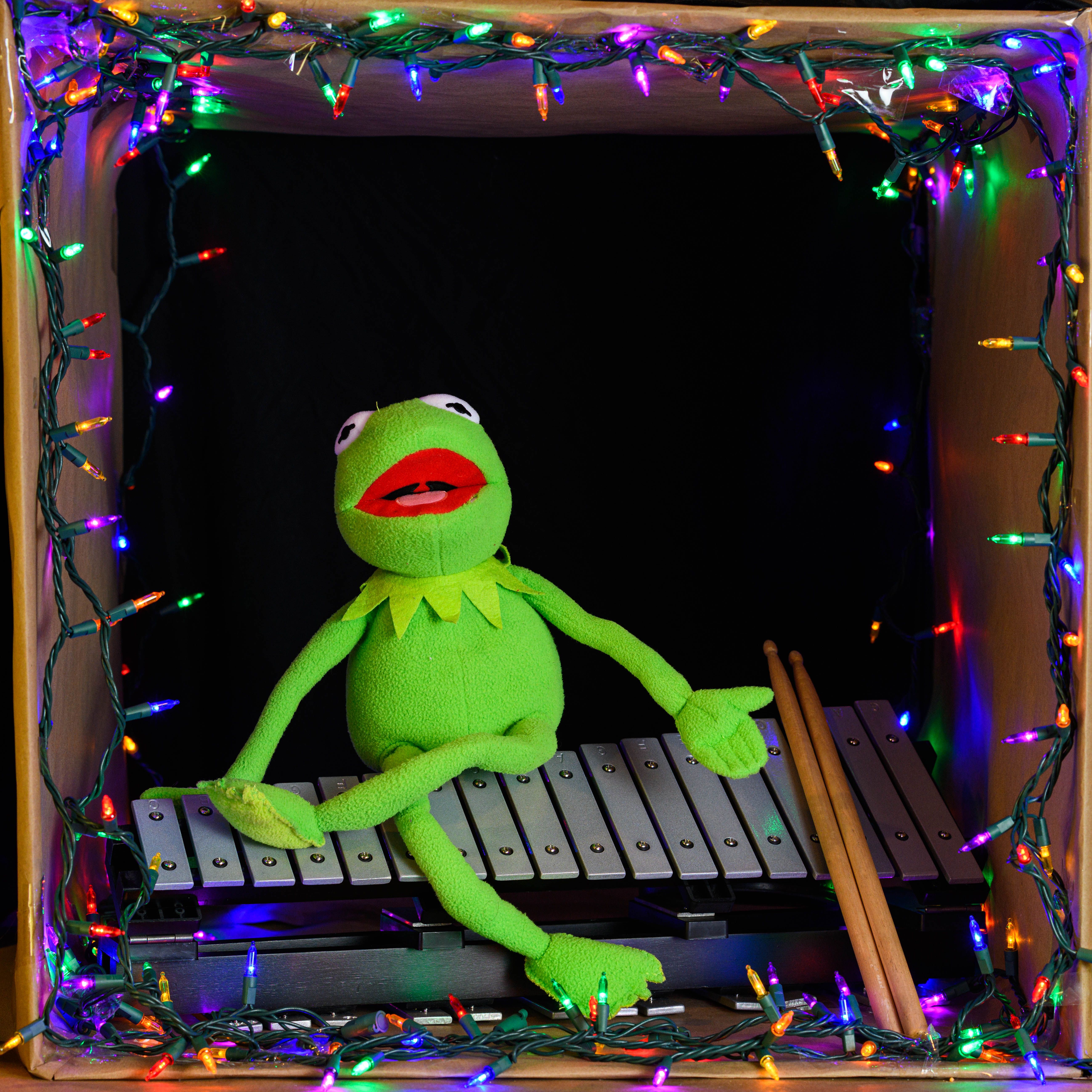 Green puppet playing xylophone surrounded by colorful fairy lights.