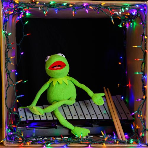 Free Green puppet playing xylophone surrounded by colorful fairy lights. Stock Photo