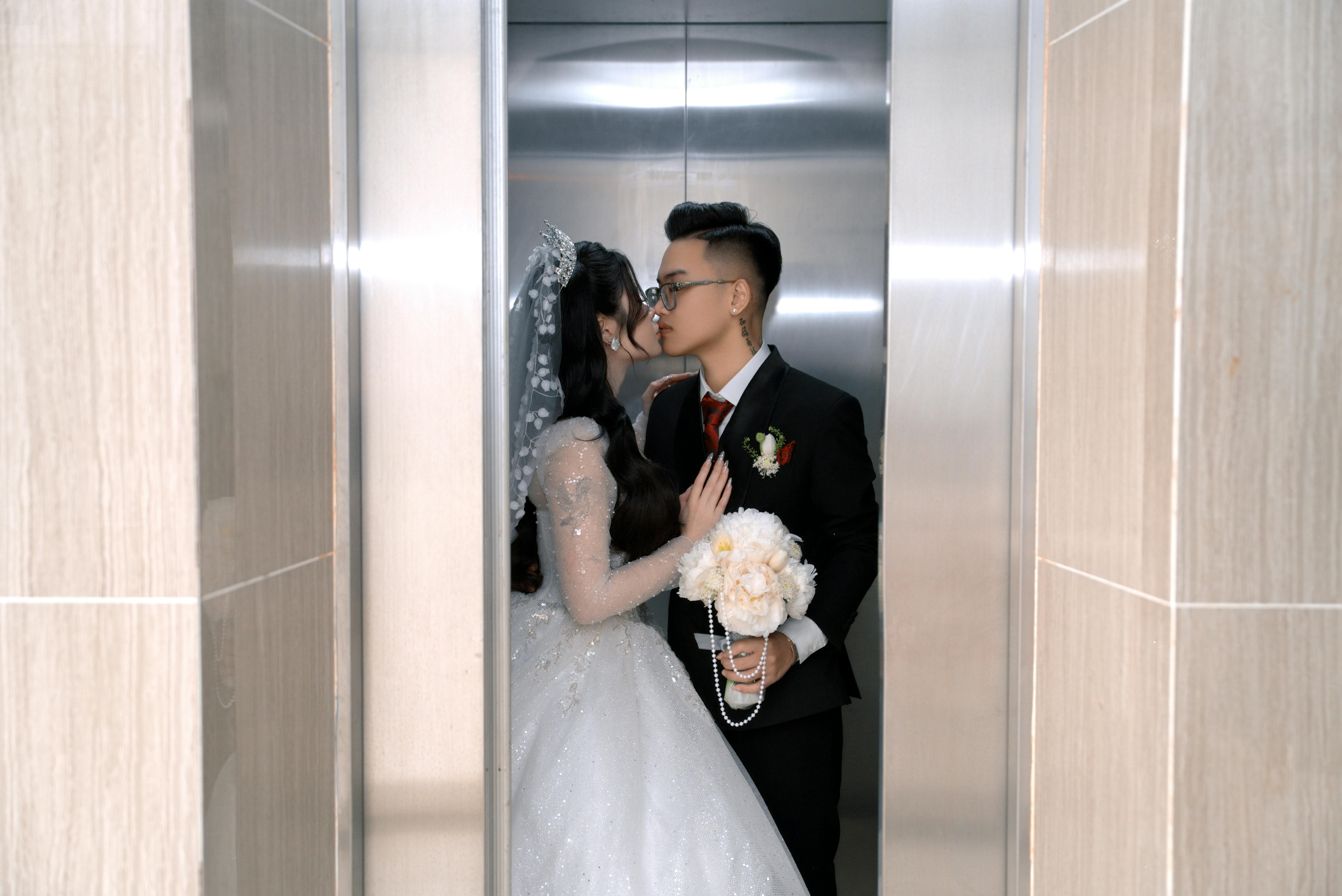 A couple sharing a romantic kiss in a wedding dress and suit inside an elevator.