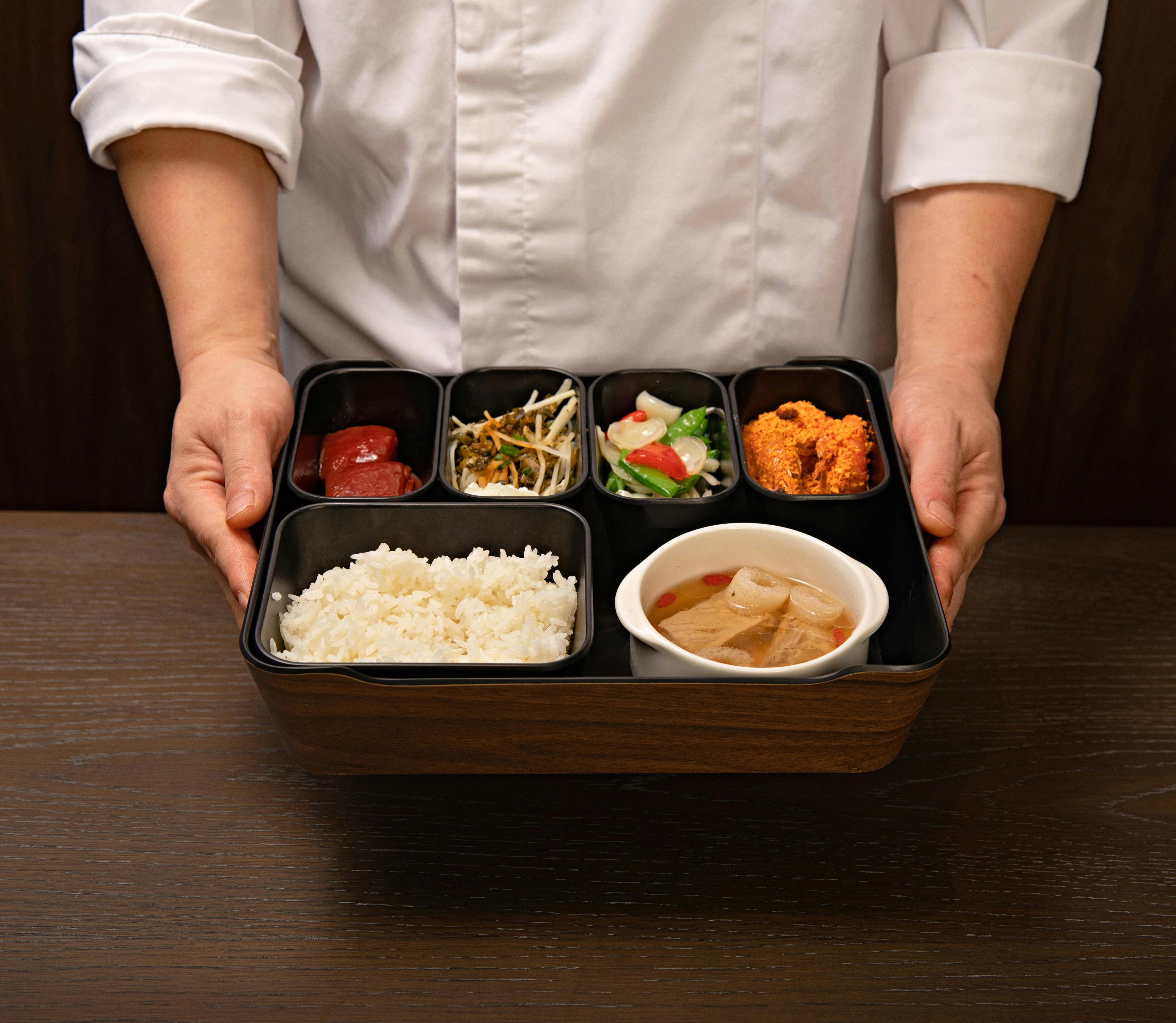 Chef presenting a traditional Japanese bento box with assorted dishes, highlighting Japanese cuisine.