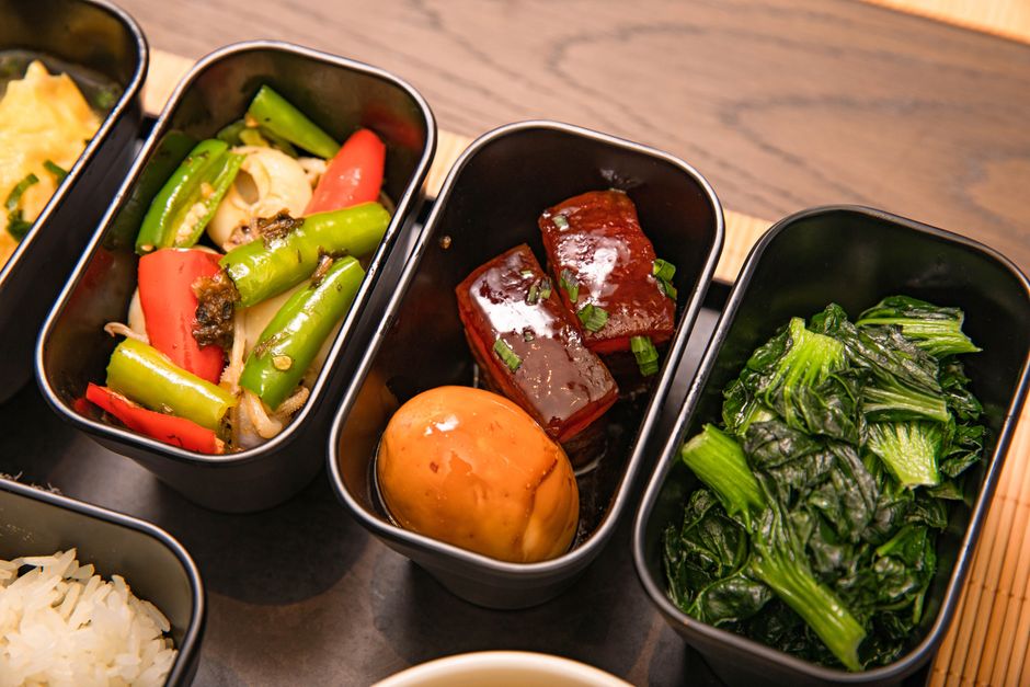 A clay pot of glossy dark brown braised pork belly cubes and whole hard-boiled eggs sitting in a thick caramel sauce, served over white rice.