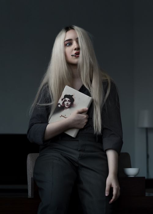 Free Blonde woman with book, dramatic lighting indoors, poised expression. Stock Photo