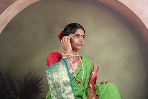 Free A woman elegantly dressed in a green saree with traditional Indian jewelry, set against a studio background. Stock Photo