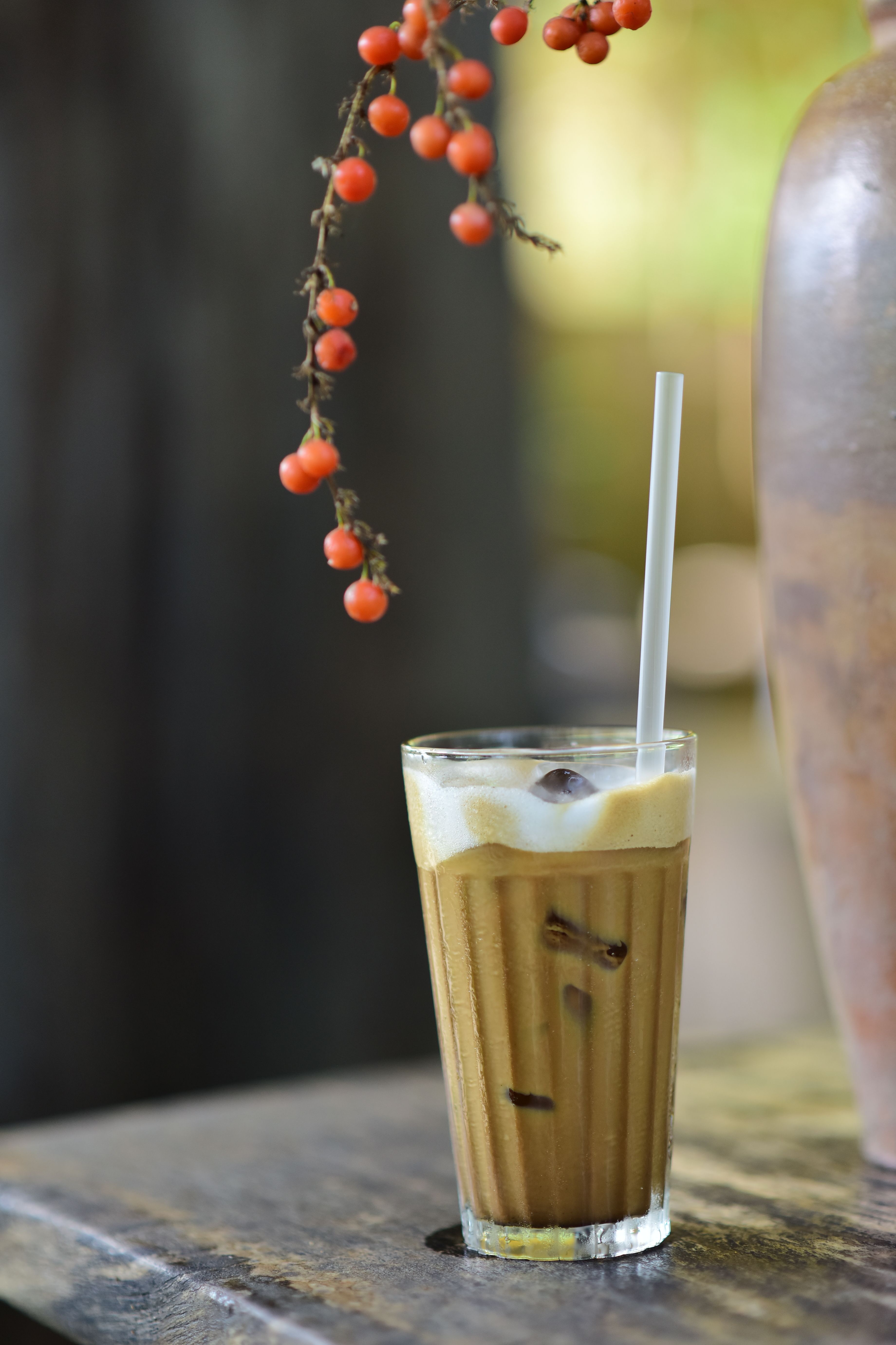 A refreshing iced coffee in a glass with ice cubes and a straw on a rustic table.