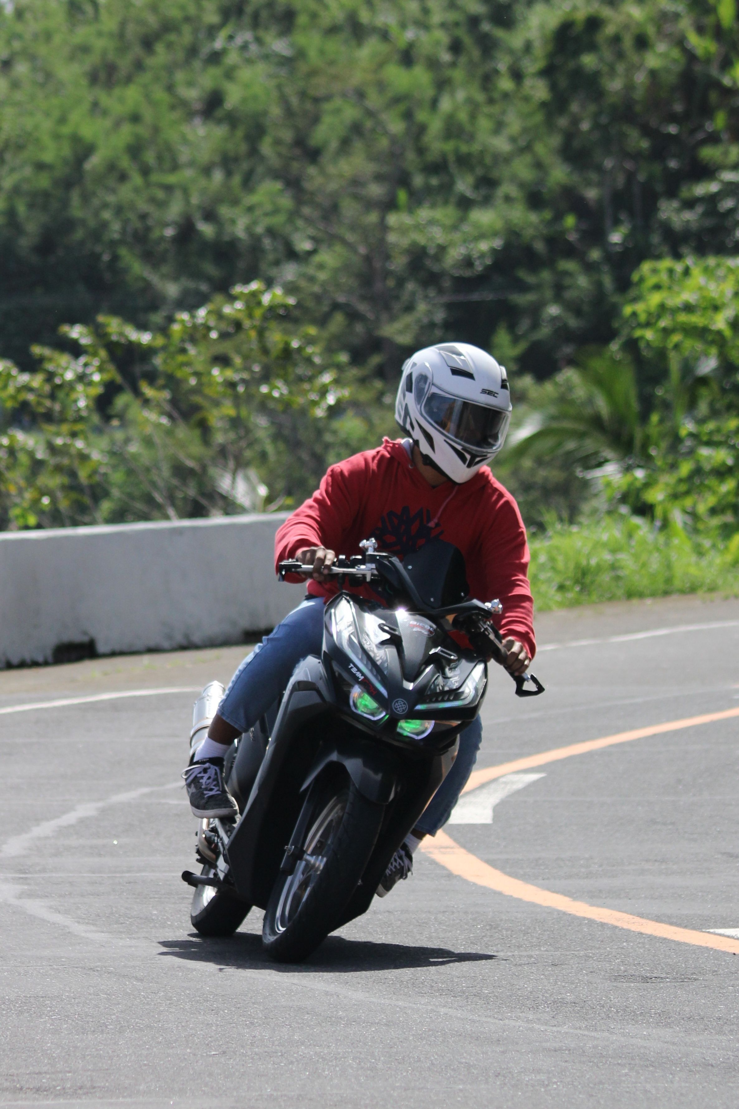 Helmeted rider on a motorcycle taking a sharp turn on a road in Sagnay, Bicol, Philippines, surrounded by greenery.