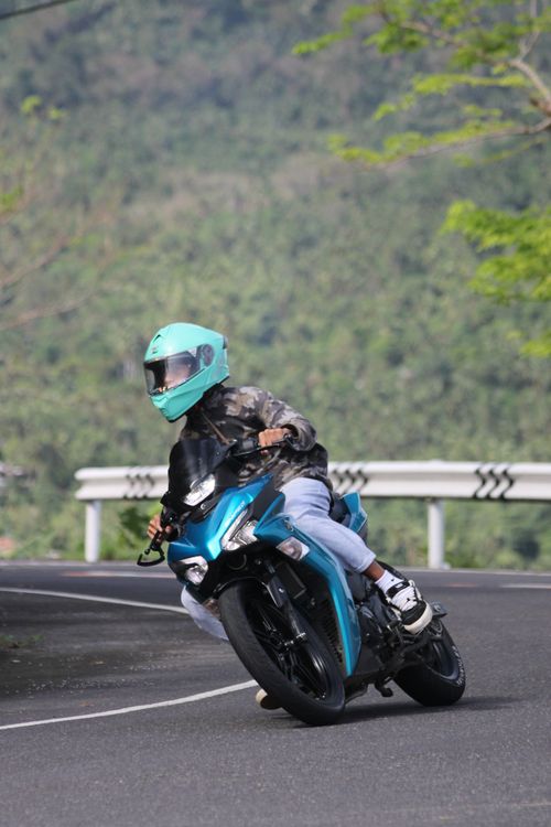 Free An adult motorcyclist leans into a sharp curve on a scenic mountain road under a clear sky. Stock Photo