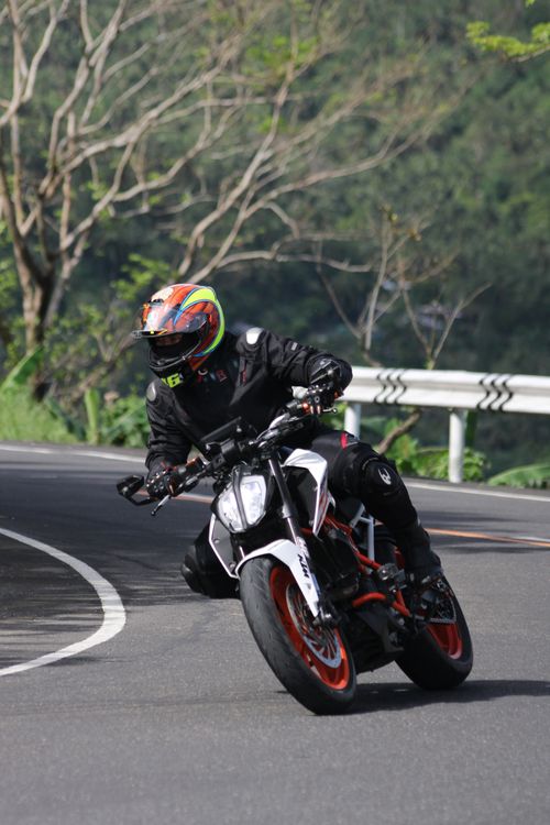 Free A motorcyclist takes a sharp turn on a scenic winding road beside lush greenery. Stock Photo