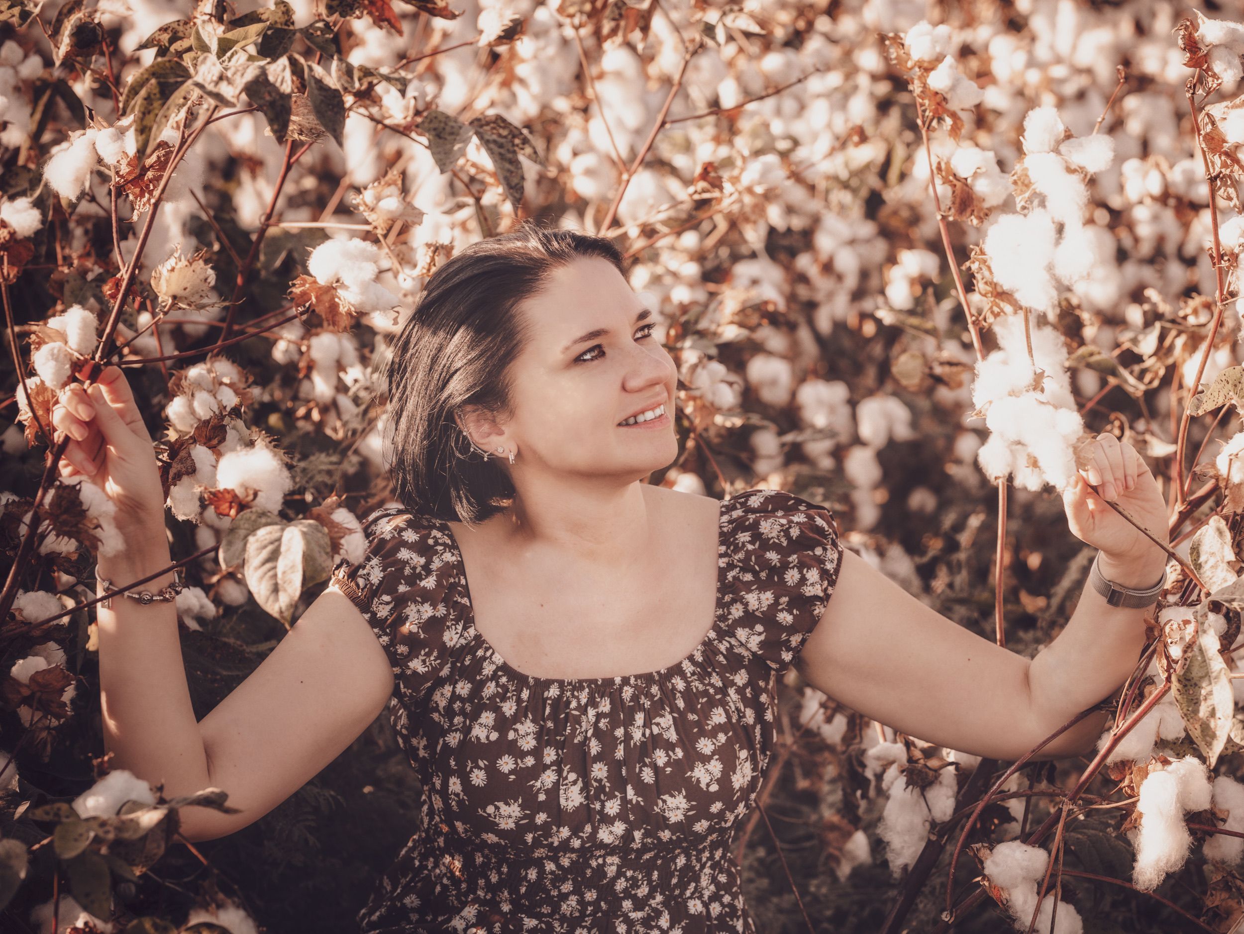 Smiling woman amidst blooming cotton field, embracing nature's beauty.