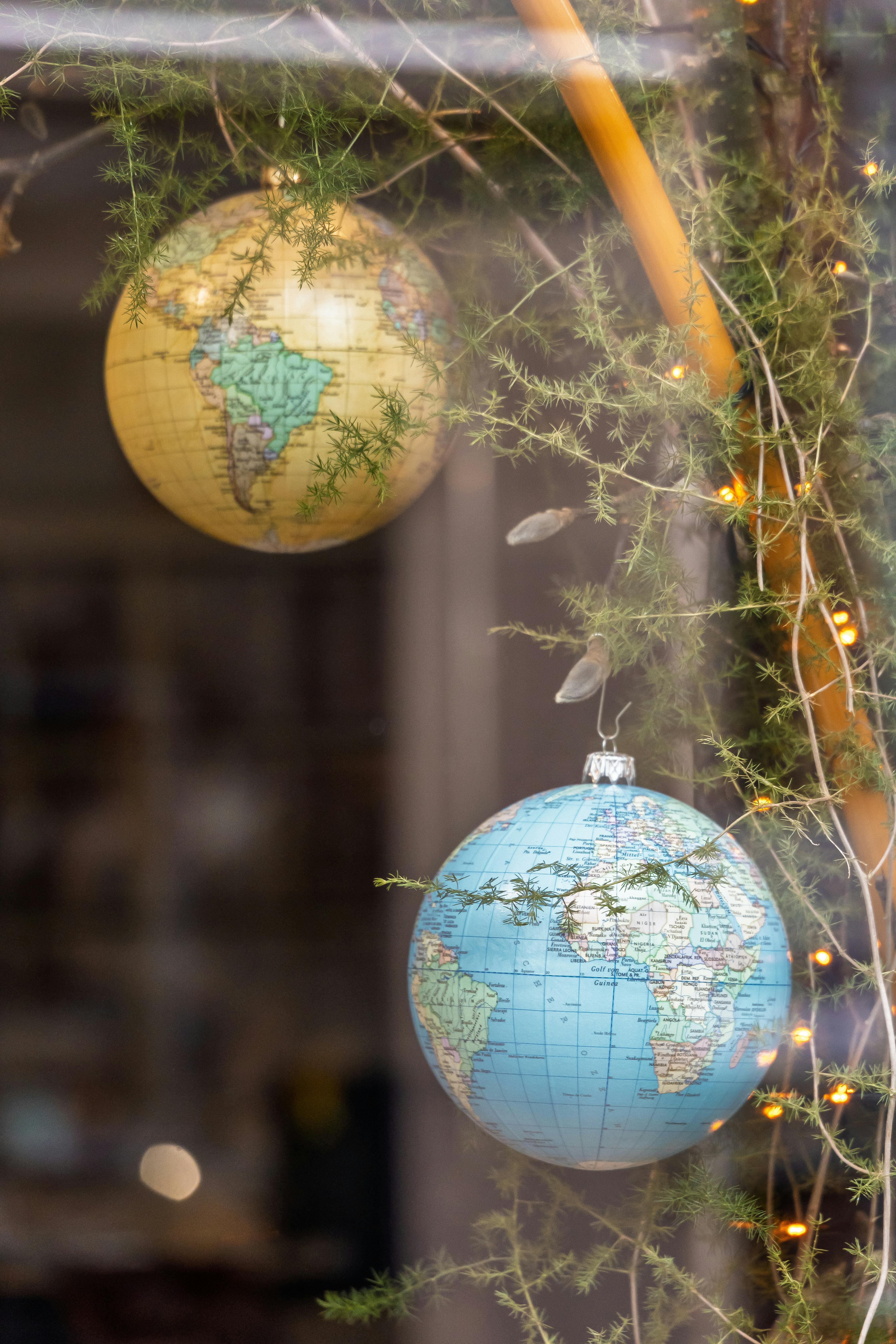 Decorative globe ornaments hanging in a festive window display with greenery and lights.