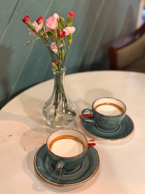 Free Cozy café scene with two coffee cups and pink carnations in a vase. Stock Photo