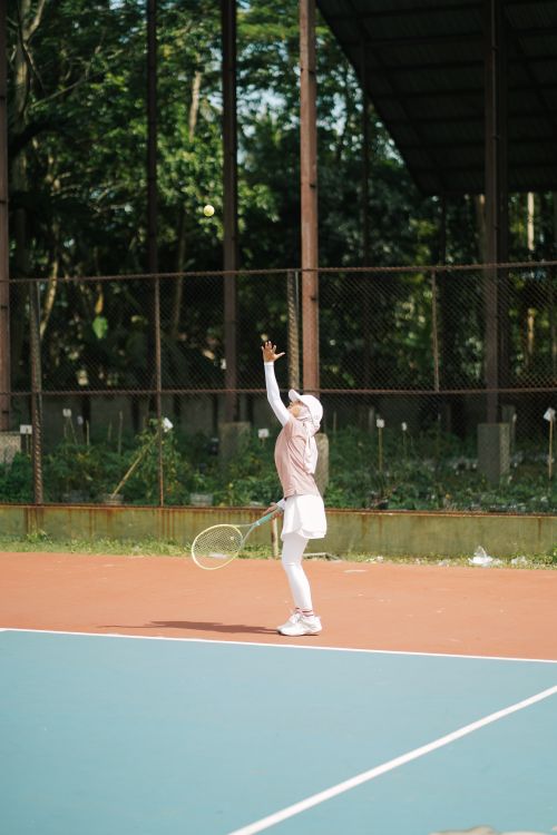 Free A young woman in sports attire serves on an outdoor tennis court surrounded by greenery. Stock Photo