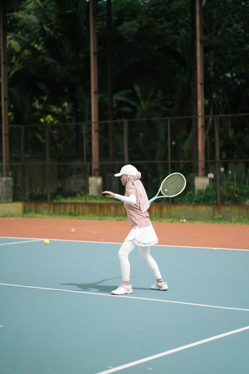 Free A young woman in hijab serves on an outdoor tennis court. Stock Photo