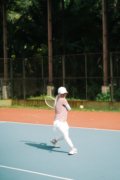 Free A young tennis player in a white cap hitting a backhand on an outdoor court. Stock Photo