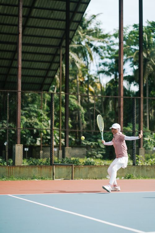 Free Tennis player hitting a forehand on a sunny day outdoors. Lush green surroundings enhance the dynamic action. Stock Photo
