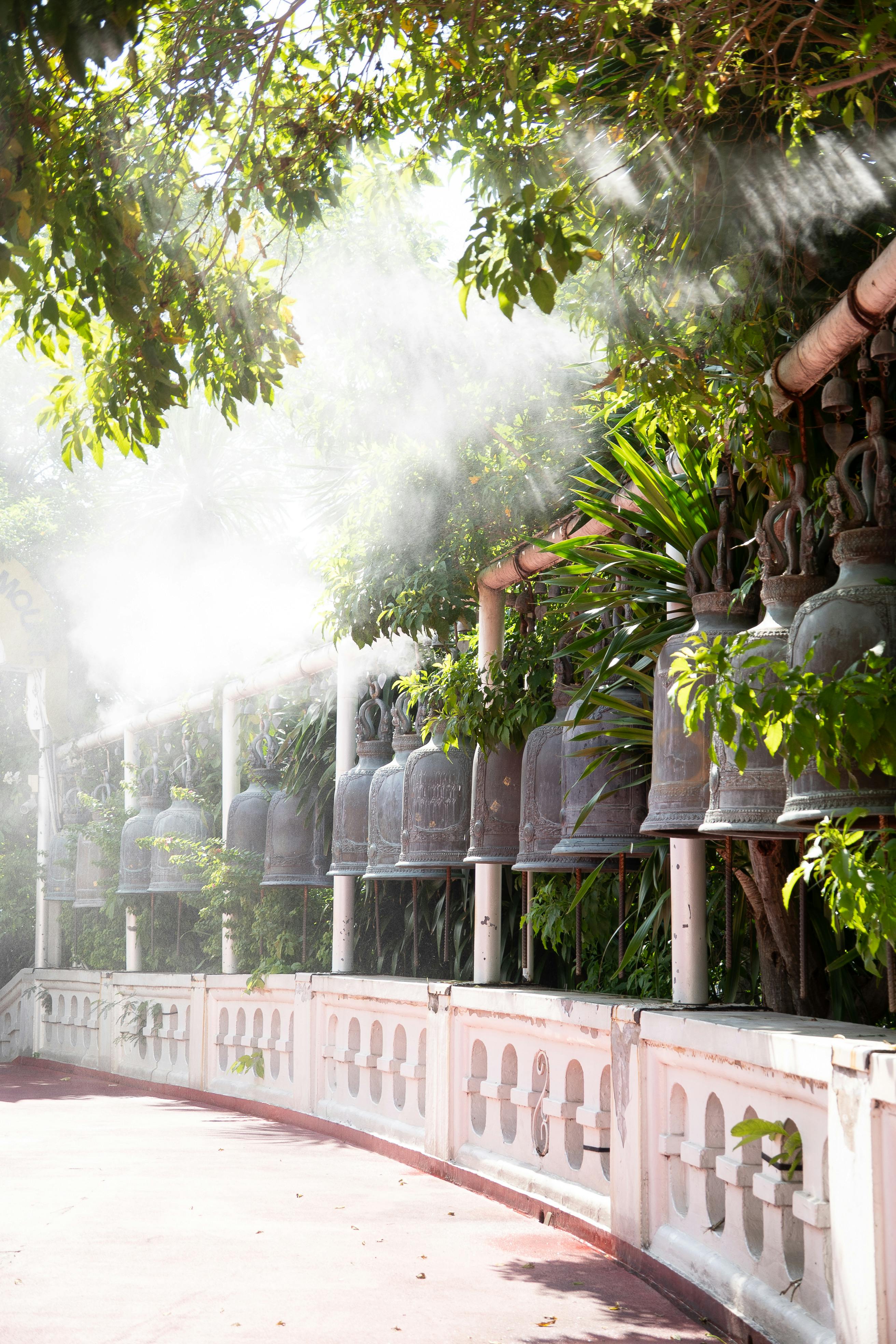 Sunlight illuminates bells on a serene temple walkway in Thailand, creating a peaceful atmosphere.
