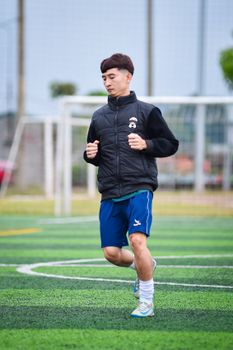 A young male football player jogging on an outdoor field in Hanoi, Vietnam.