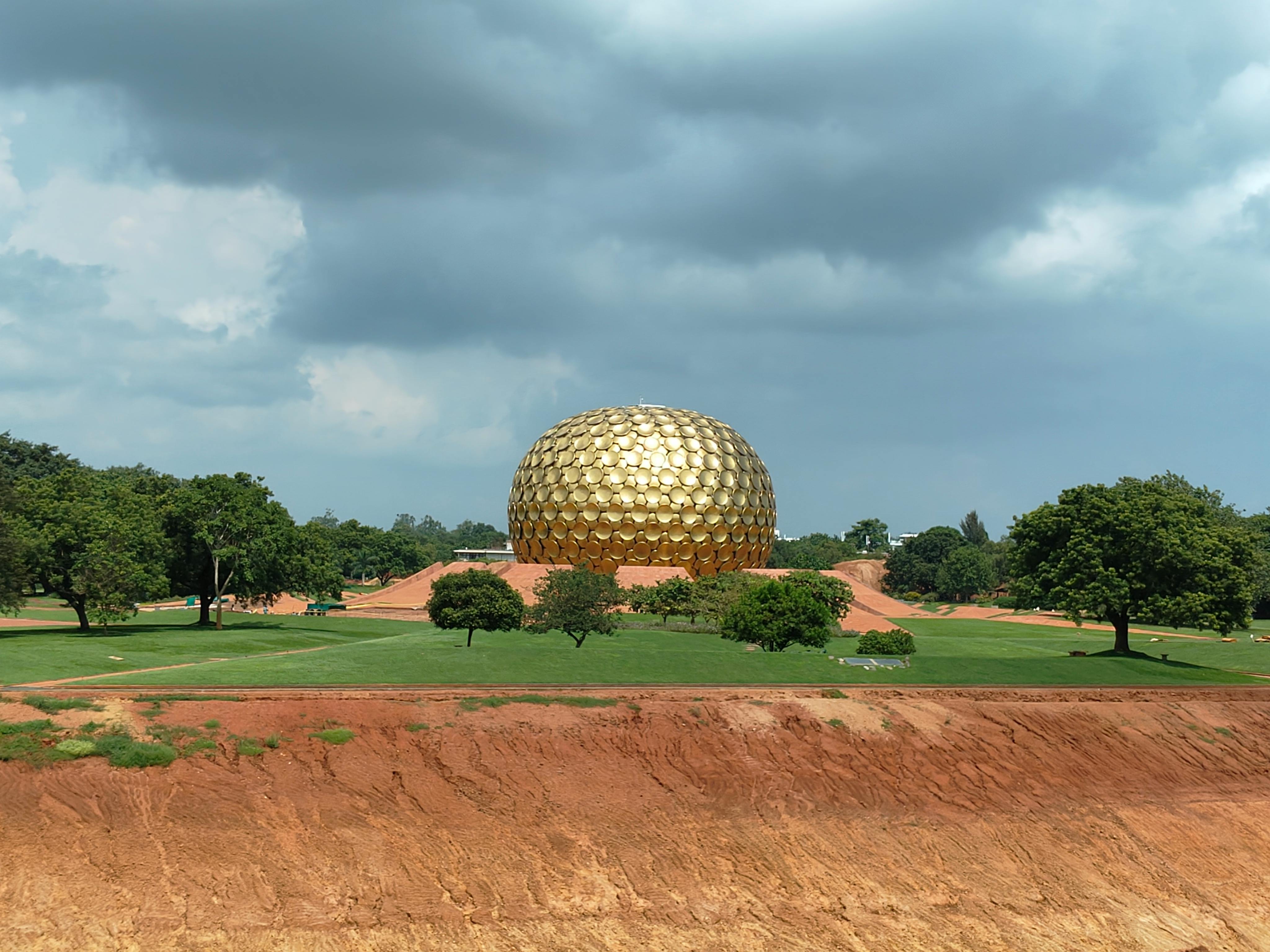 Stunning view of the golden Matrimandir in Auroville, under a dramatic sky.