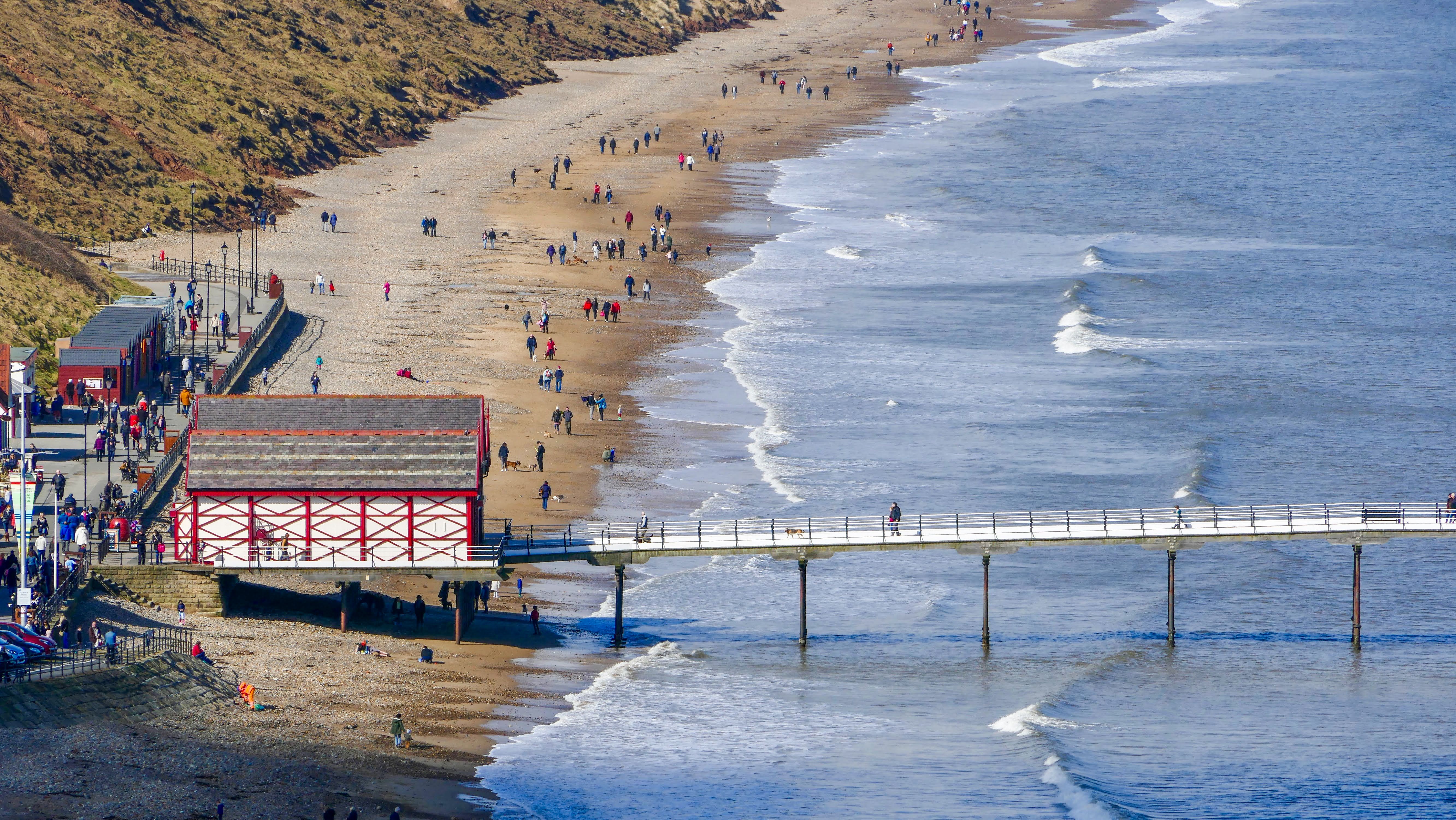 Aerial view of Saltburn-by-the-Sea's pier and beach with visitors enjoying a sunny day.