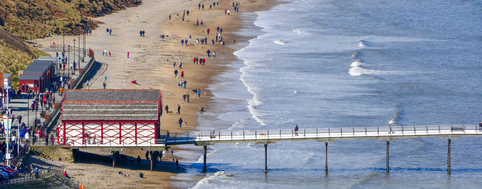 Aerial view of Saltburn-by-the-Sea's pier and beach with visitors enjoying a sunny day.