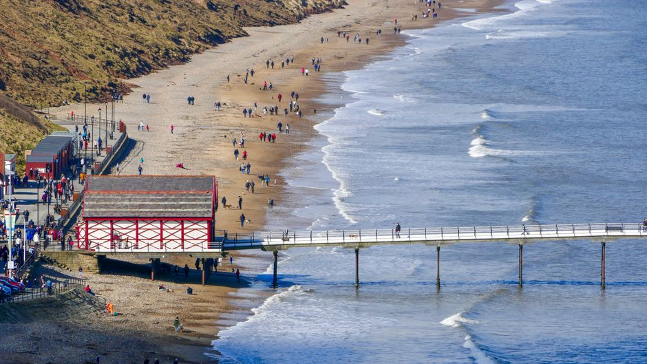 Aerial view of Saltburn-by-the-Sea's pier and beach with visitors enjoying a sunny day.