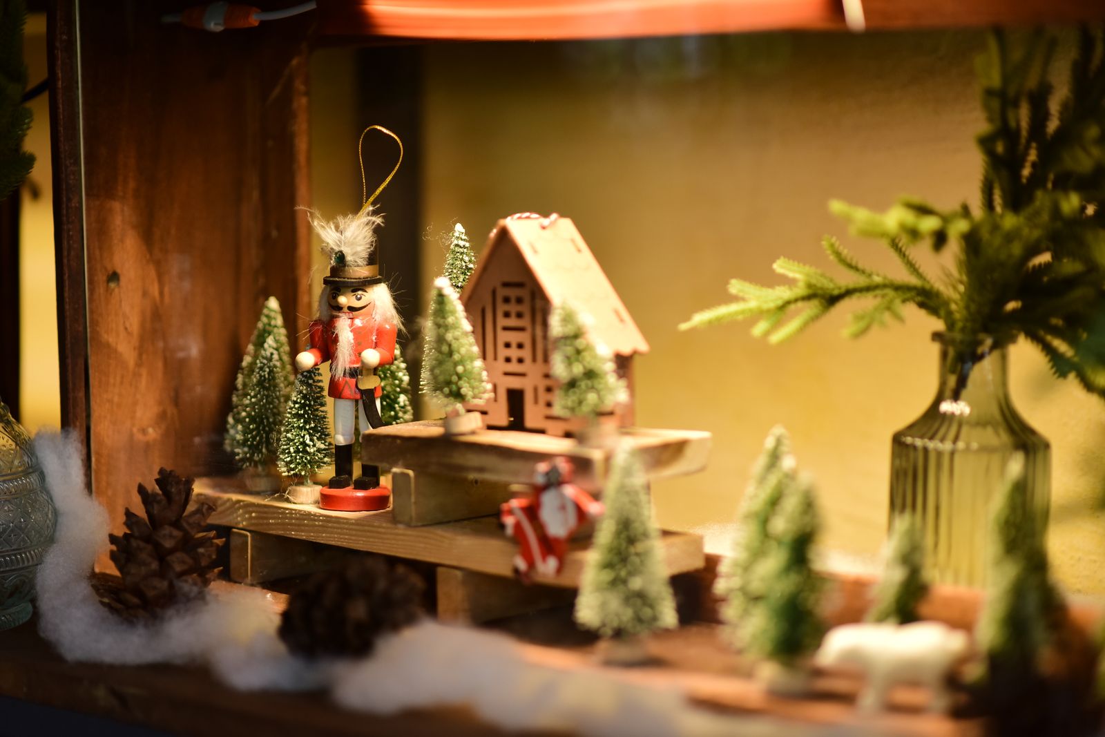 miniature Christmas village display with a nutcracker, a small house and bottle-brush trees on a shelf