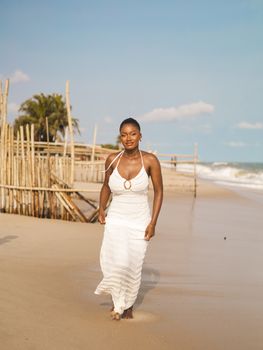 Woman in a white dress strolling on a sunny beach, capturing a serene and stylish moment.