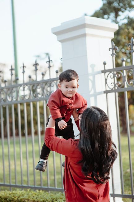 A joyful moment of a mother lifting her baby outdoors in a park.