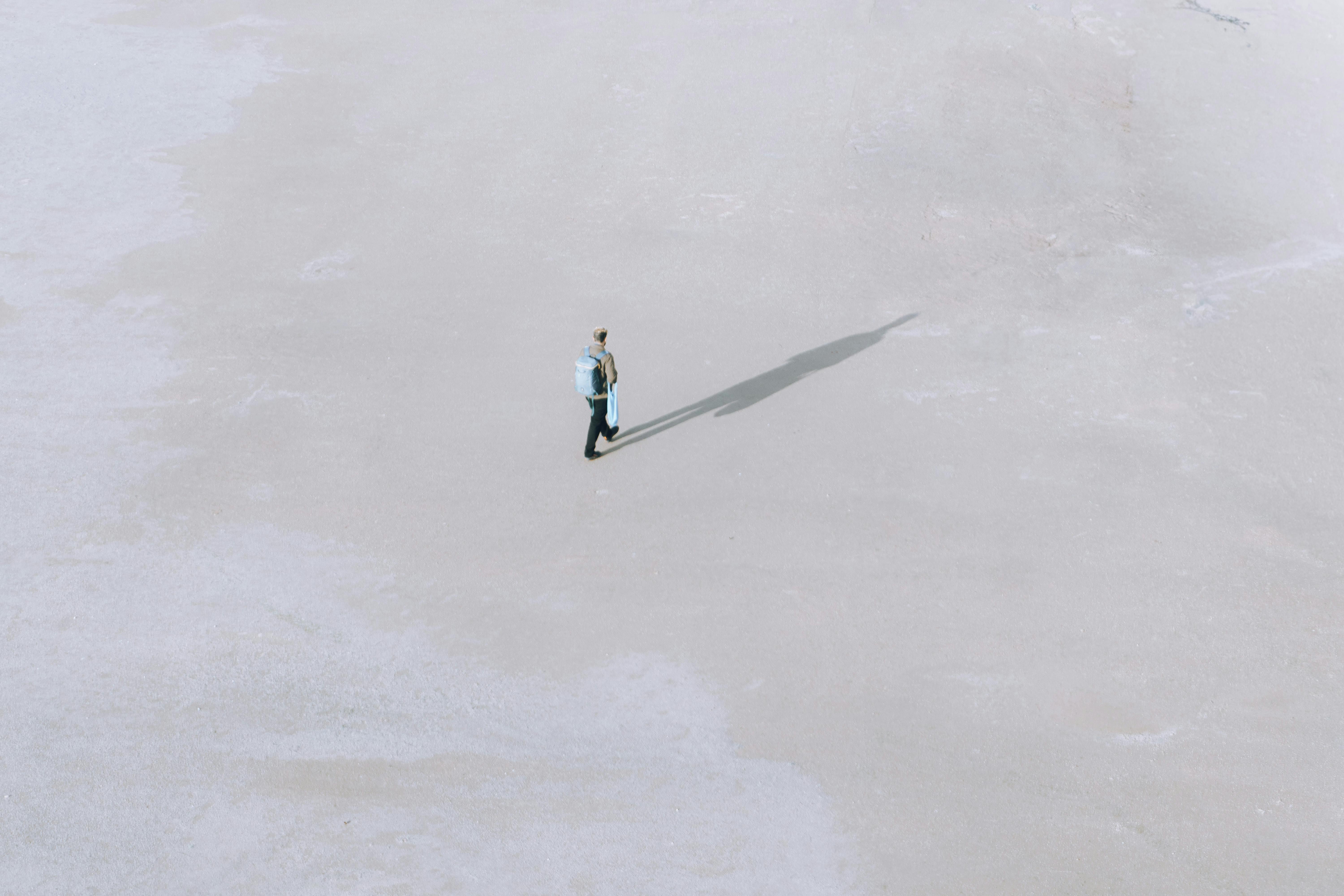 A lone traveler with a backpack casts a long shadow on a vast, minimal landscape in Istanbul.