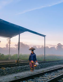 A woman in traditional attire walks on railway tracks surrounded by morning mist.