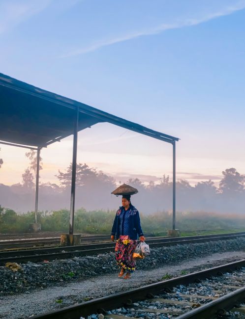 A woman in traditional attire walks on railway tracks surrounded by morning mist.