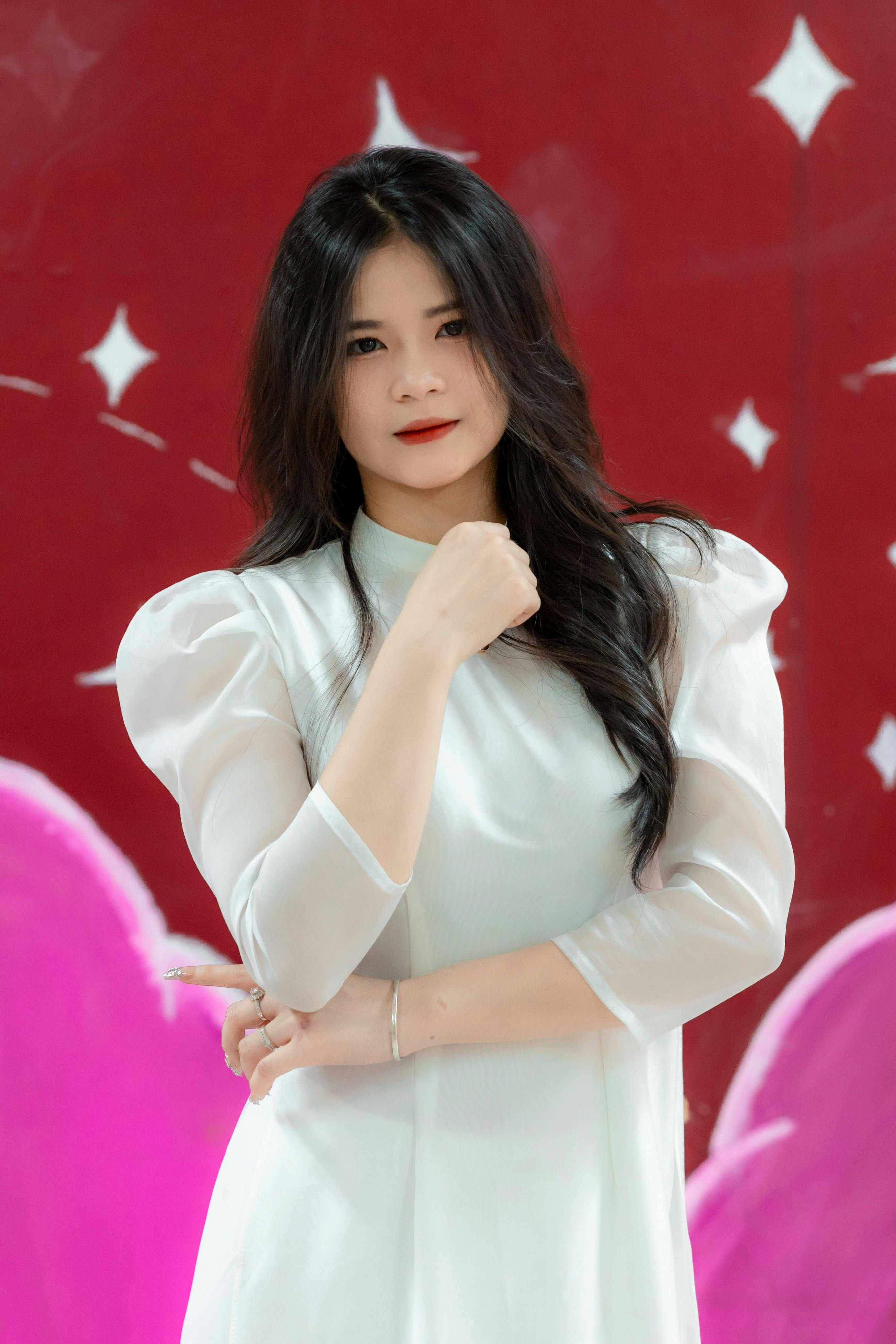 Portrait of a woman in a white dress posing confidently with a red artistic background.