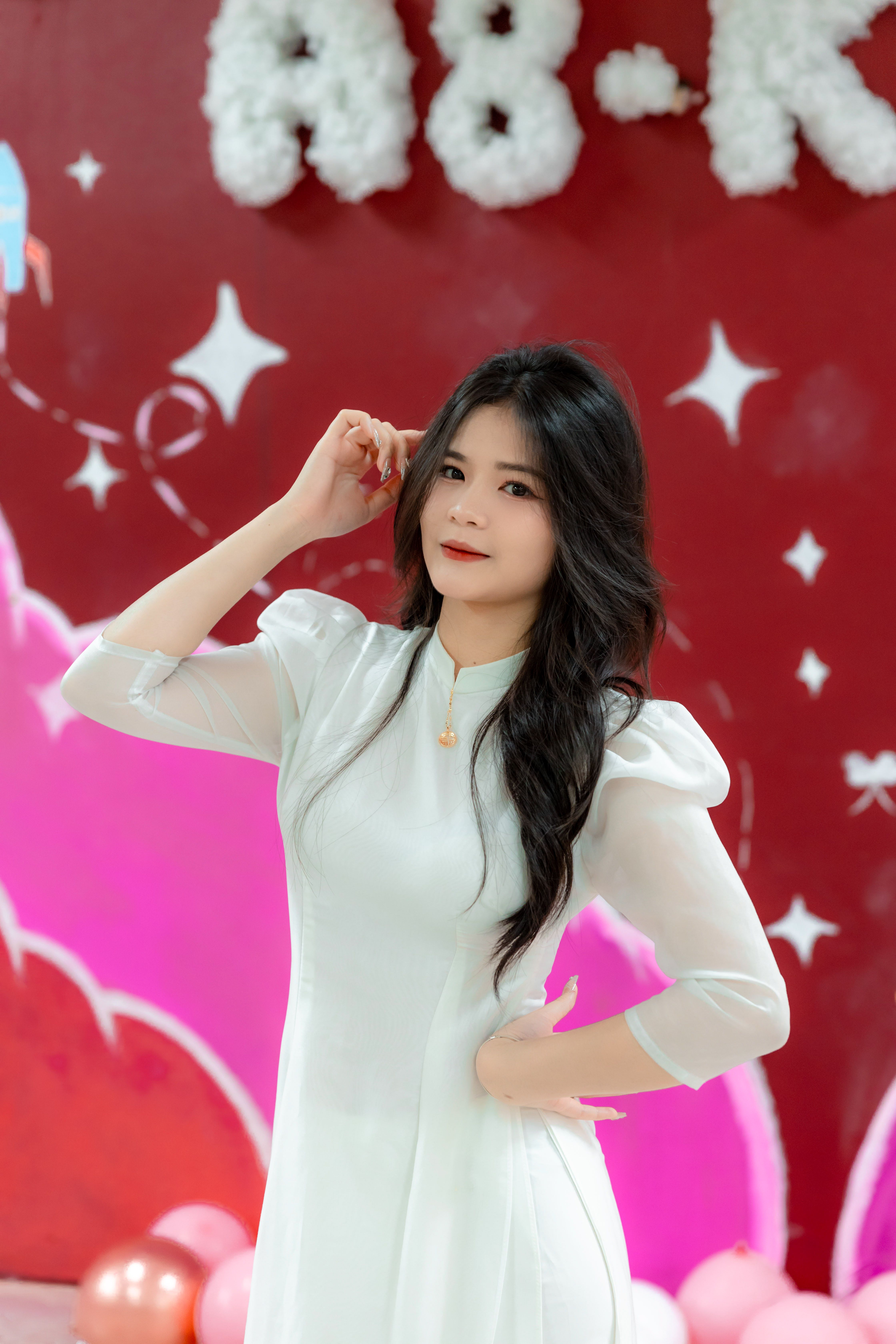 Elegant woman poses in traditional white ao dai, vibrant backdrop.