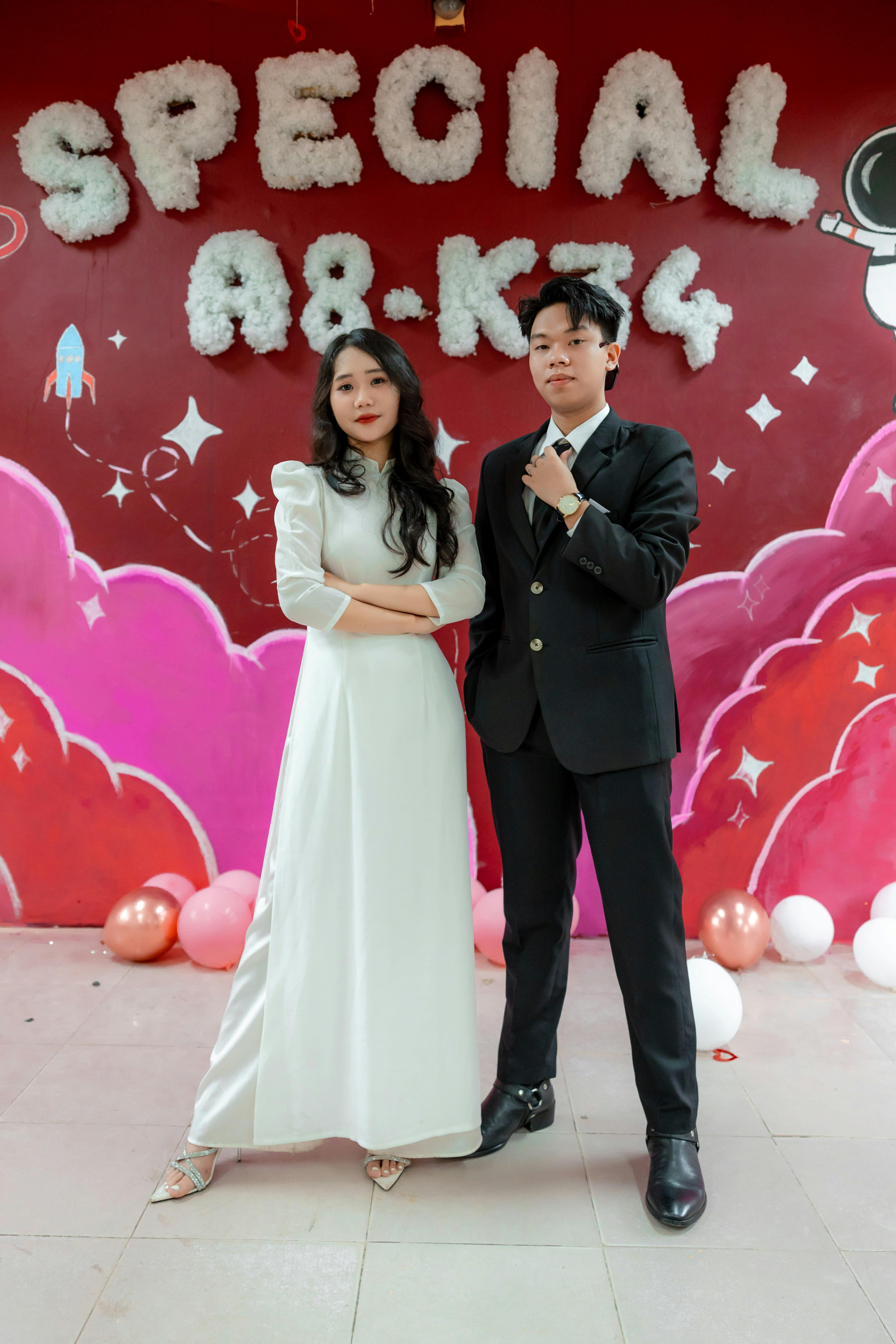 A couple dressed formally poses in front of a vibrant event backdrop.
