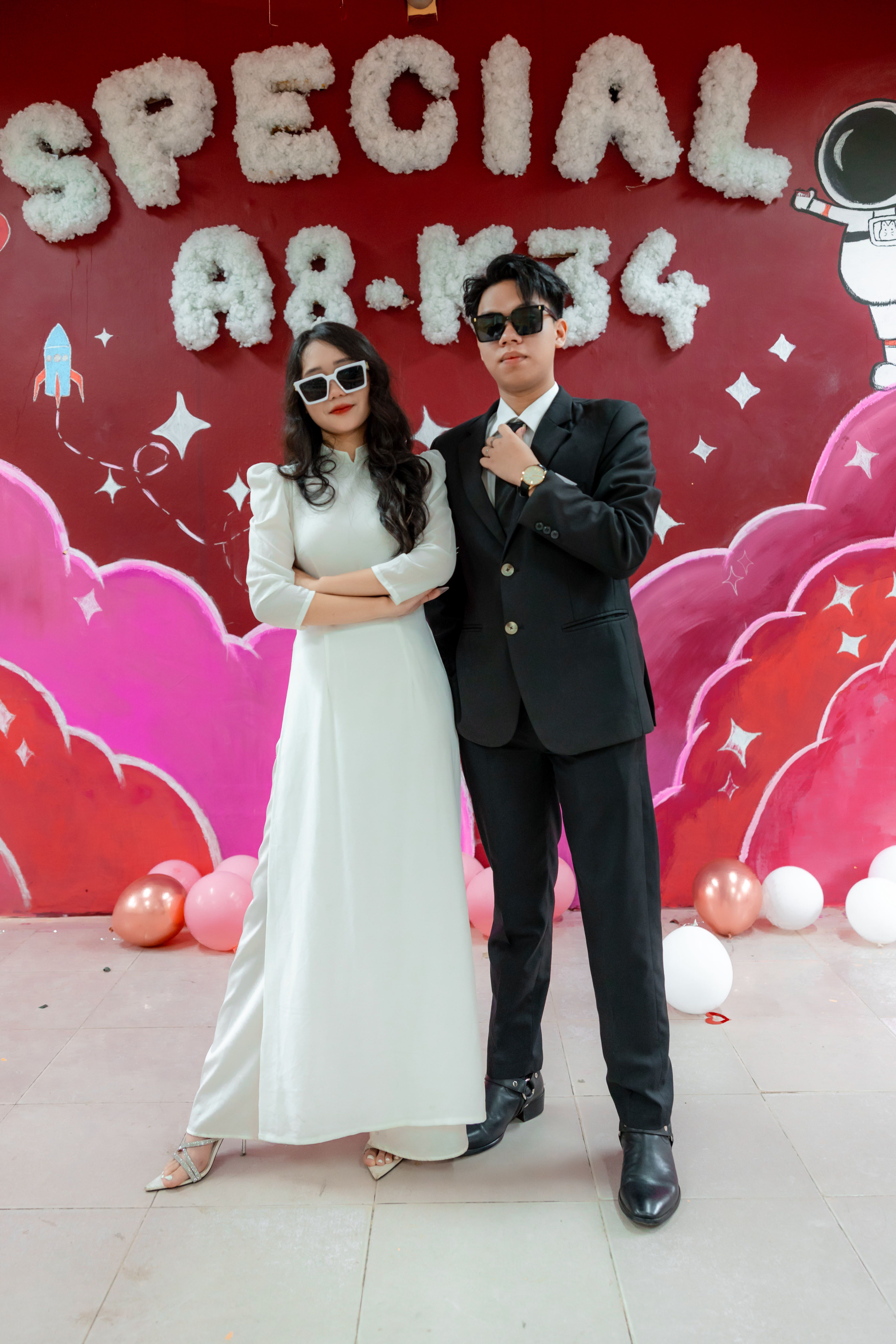 Young couple in formal wear posing with sunglasses at a vibrant celebration.