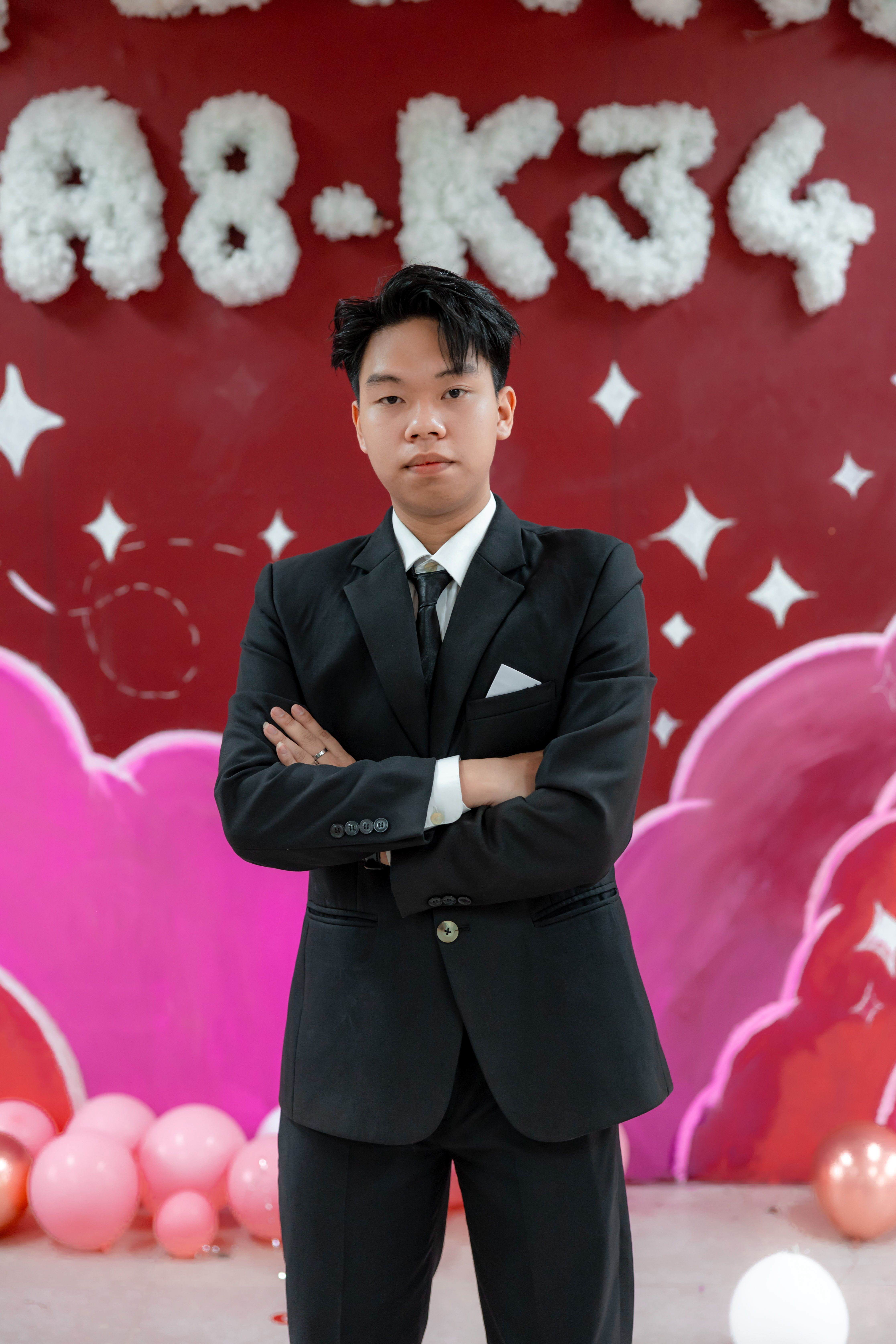 Confident young man in a black suit poses against a creative red background.