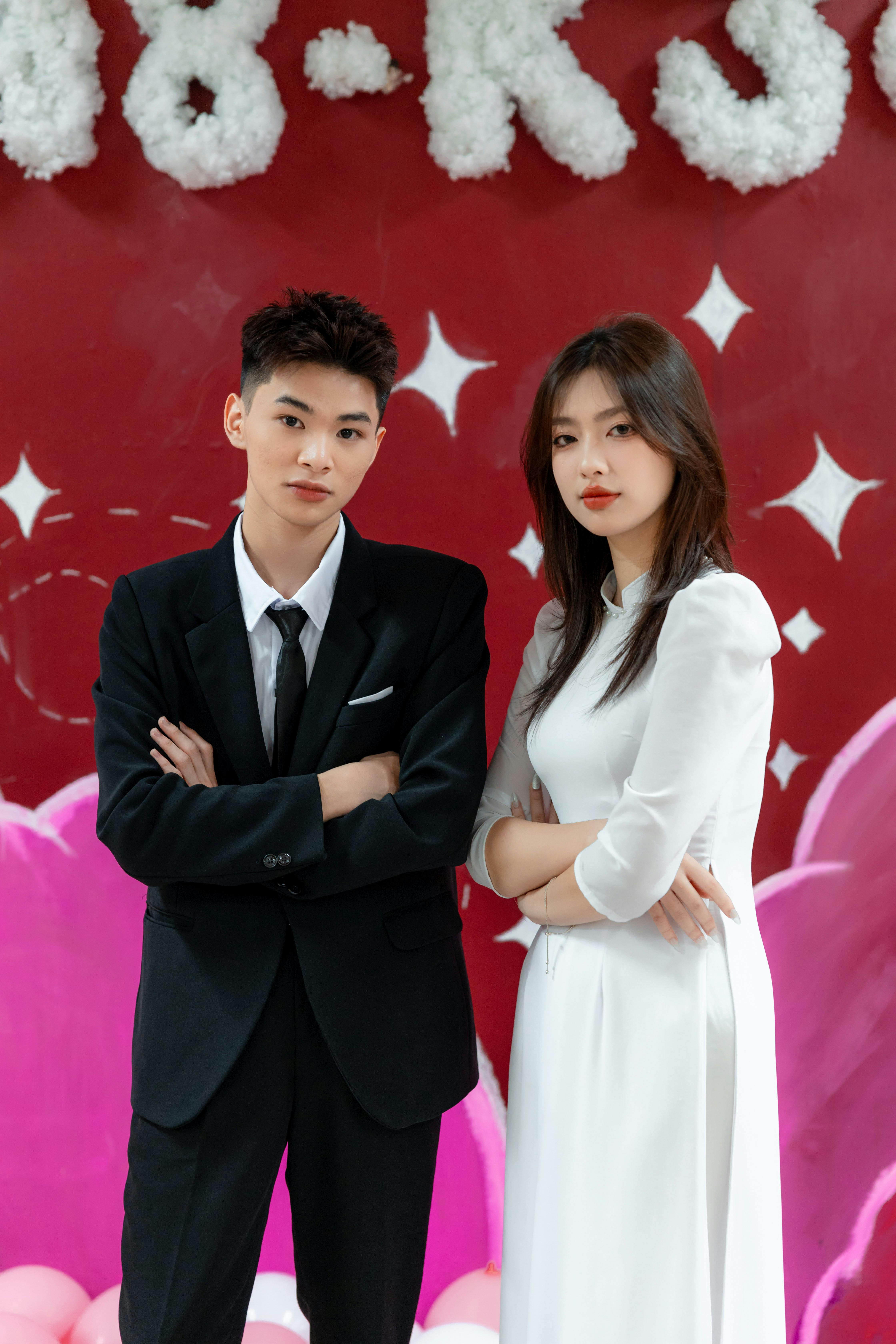 Stylish couple posing confidently at a formal event against a vibrant red backdrop.