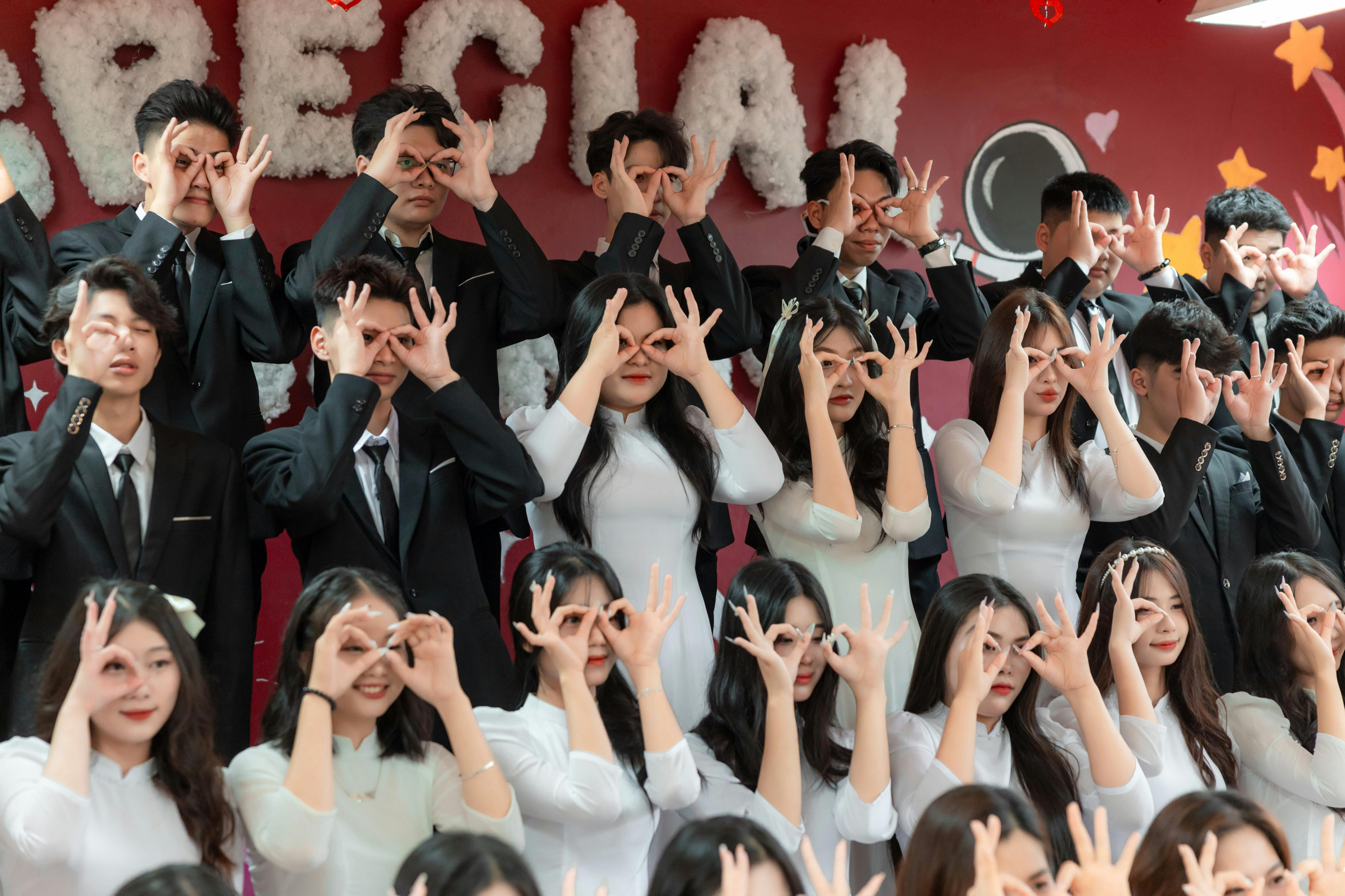 A diverse group of young adults in formal attire at a celebratory event making playful gestures with their hands.