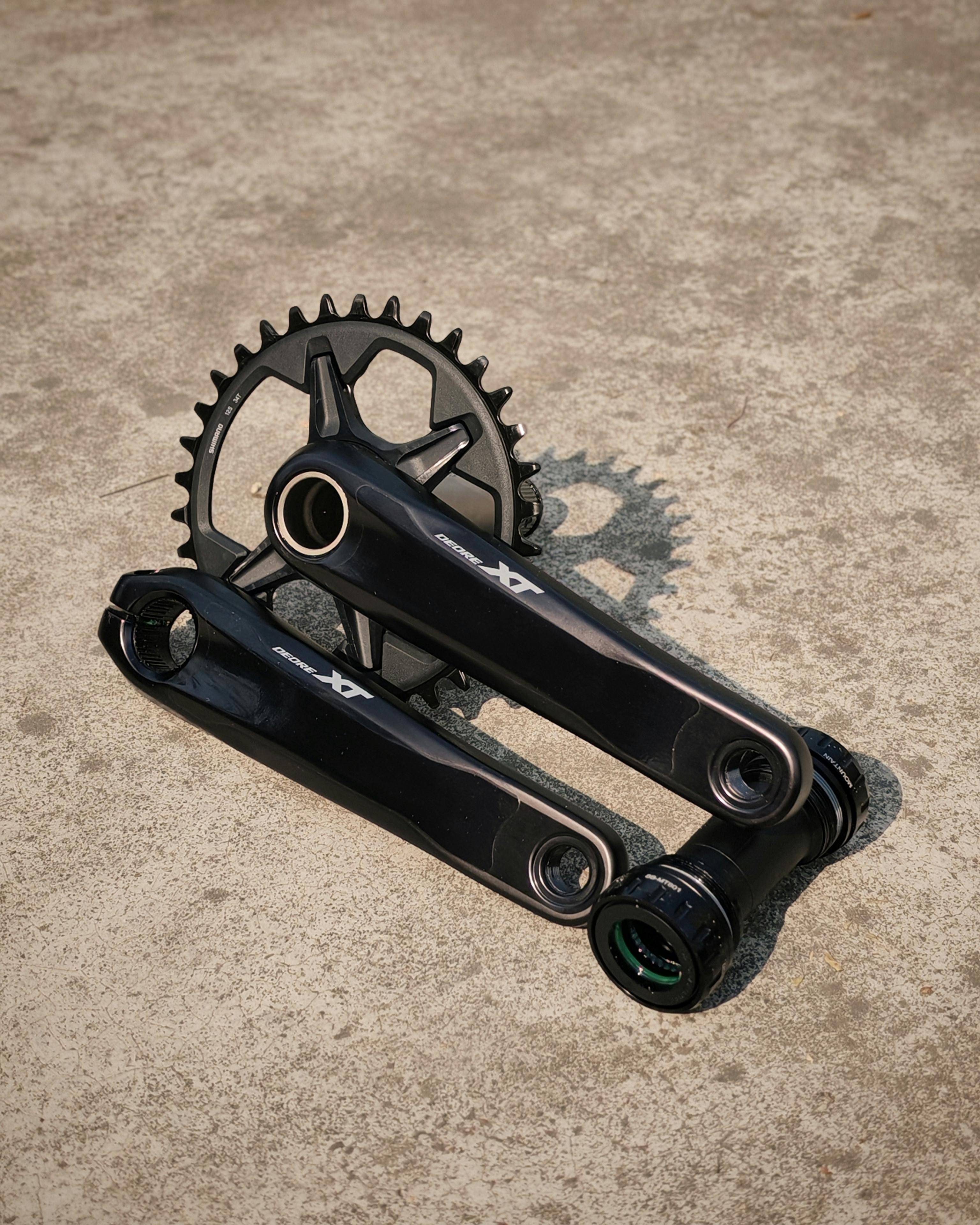 Detailed view of a bicycle crankset and chainring on a textured concrete floor.