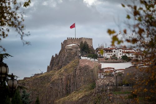 Free Scenic view of Ankara Castle with a Turkish flag flying atop, surrounded by fall foliage and historic homes. Stock Photo